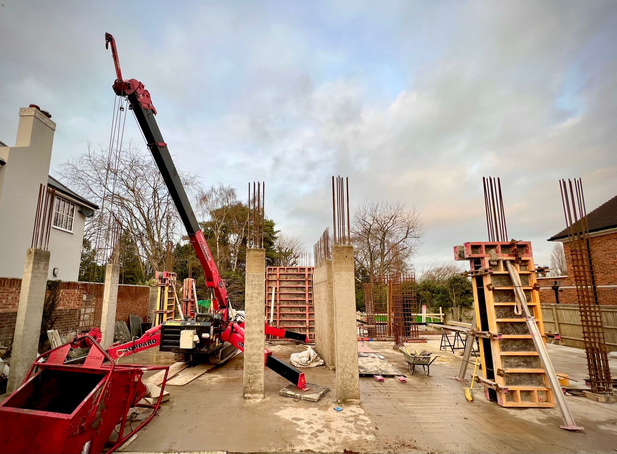Red crane lifting steel reinforcement with cast concrete columns and formwork on site at Virginia Water